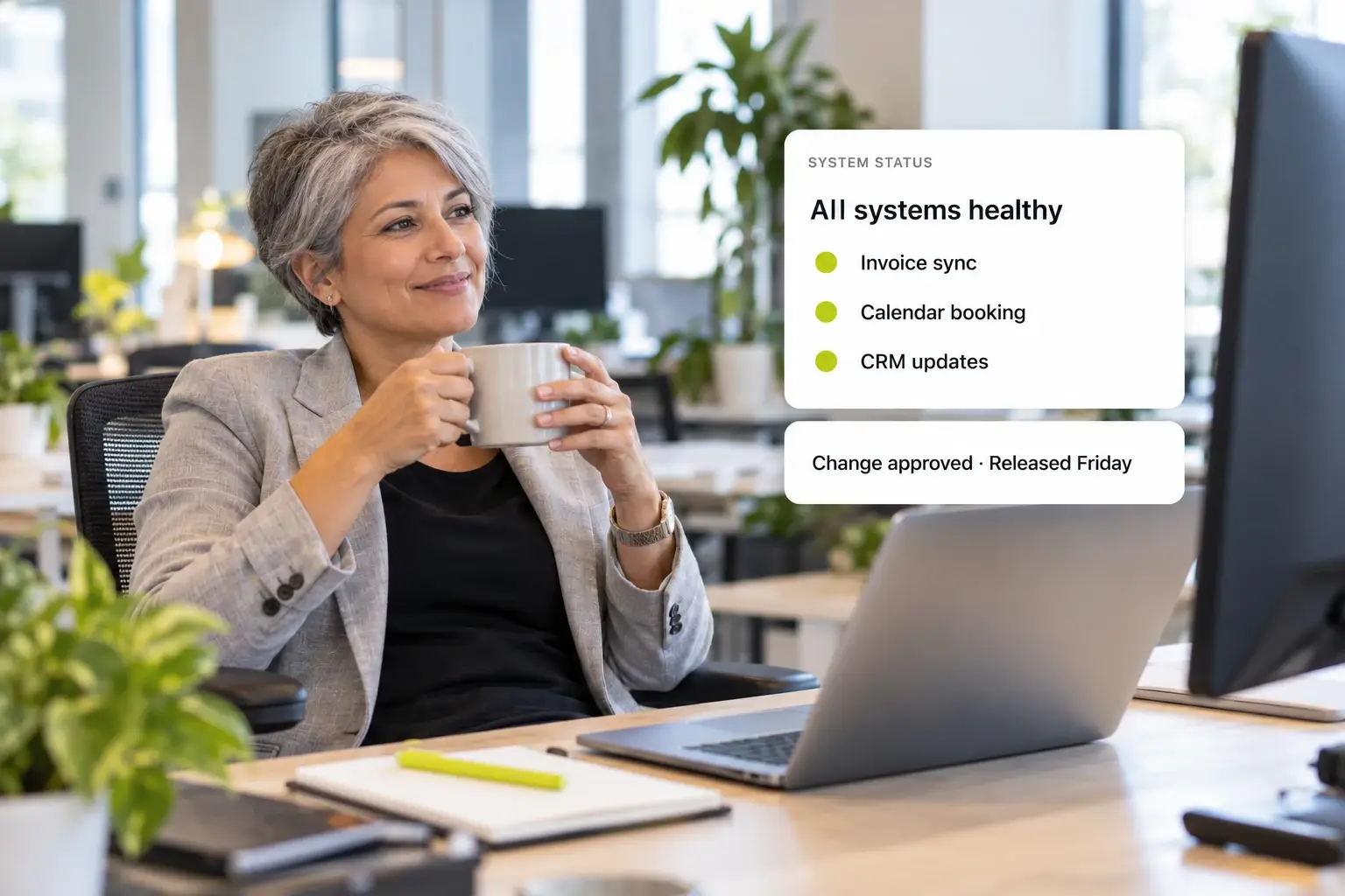 An IT and operations lead relaxes at her desk with a coffee while a system status panel shows invoice sync, calendar booking, and CRM updates all healthy, and an approved change released Friday.